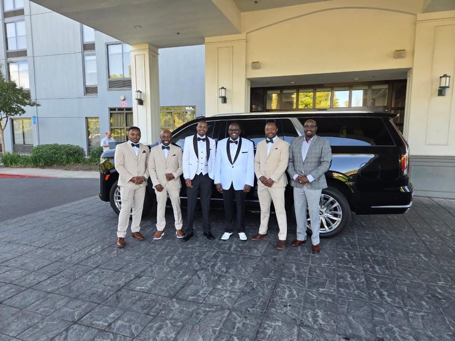 A group of men in tuxedos are standing in front of a limousine.