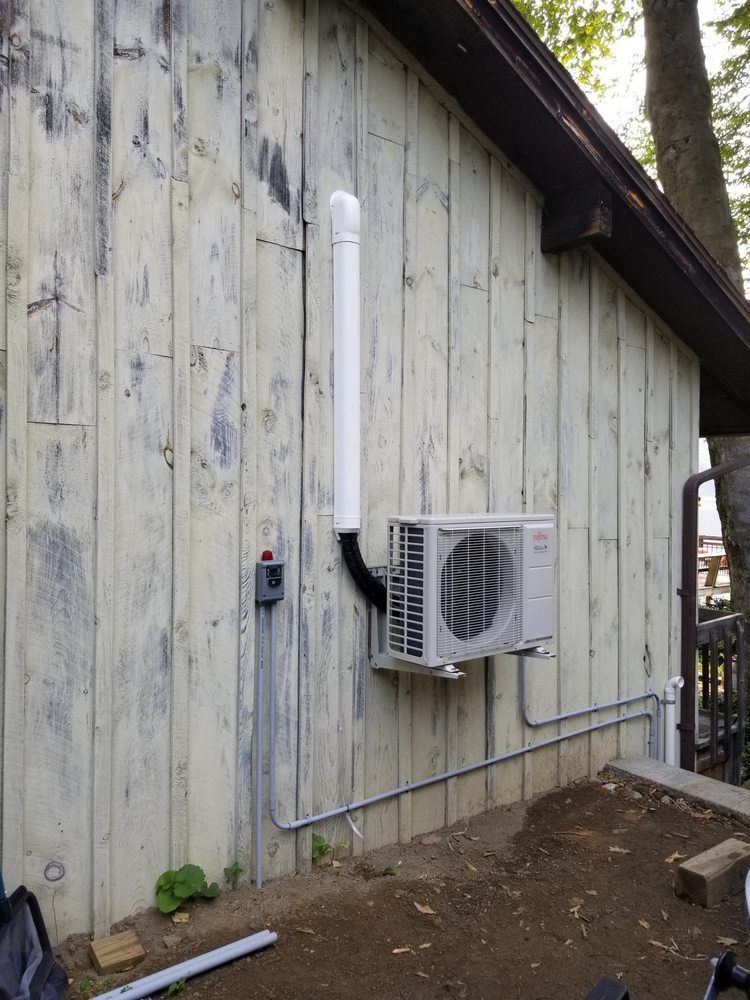 A white air conditioner is mounted on the side of a wooden building.