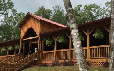 Wooden cabin-style lodge with porch and hanging ferns in a wooded setting