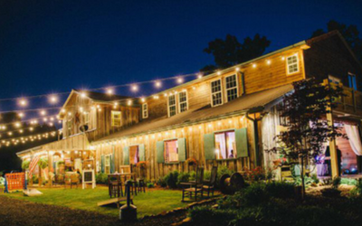 Lit rustic building with string lights and glowing windows at night, viewed from a grassy lawn.