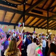 Crowd dancing indoors under wooden beams, waving colorful glowing lights in a festive celebration