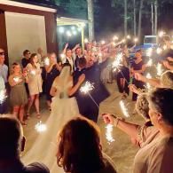 Outdoor nighttime wedding celebration with guests holding sparklers around a couple