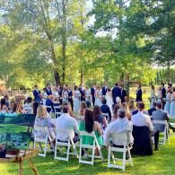 Guests seated outdoors at a wedding ceremony in a sunny, tree-lined park