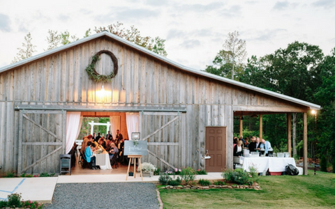 Rustic barn venue with guests gathered inside at a wedding reception, string lights glowing at sunset.