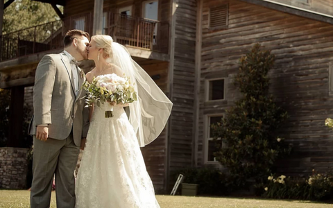 Bride and groom kissing outdoors beside a rustic wooden barn