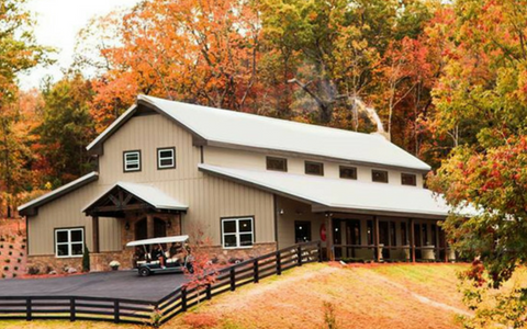 Tan barn with porch beside a road, surrounded by autumn trees with orange and red leaves.