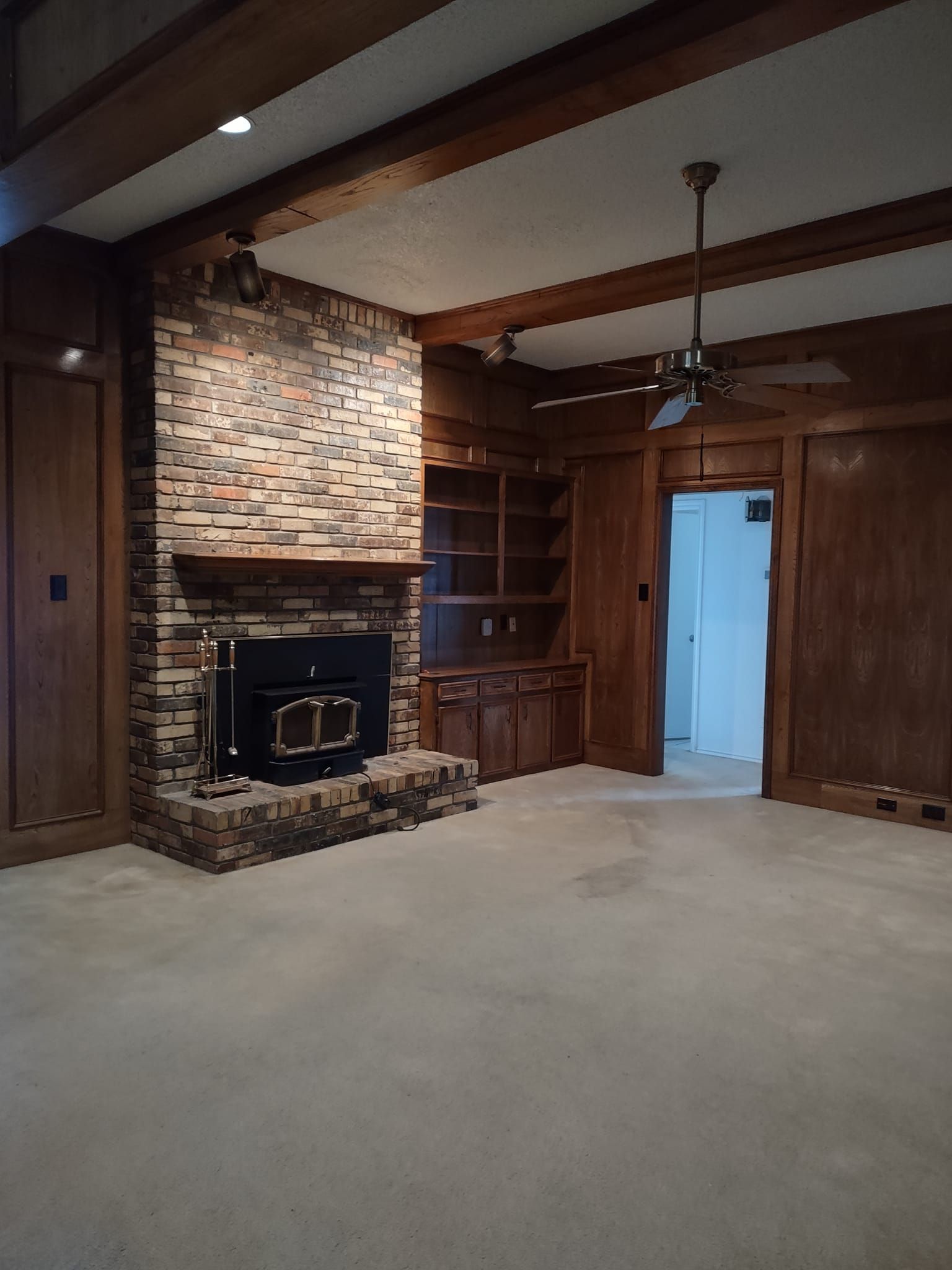 A living room with a brick fireplace and a ceiling fan