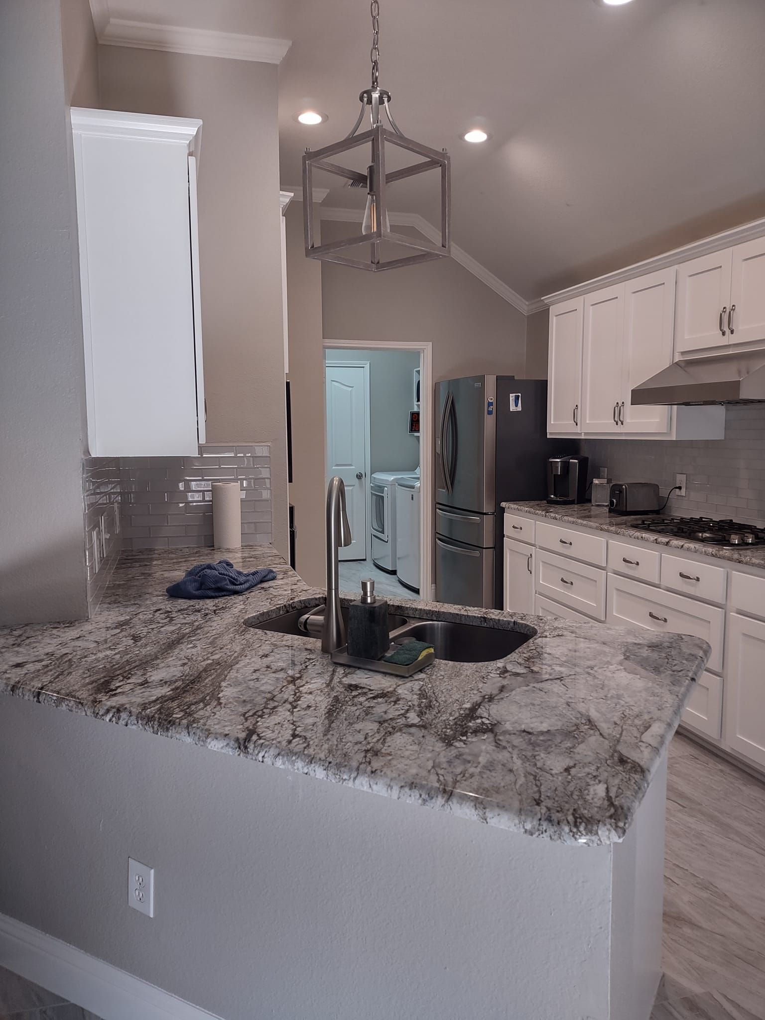 A kitchen with granite counter tops , white cabinets , a sink and a refrigerator.