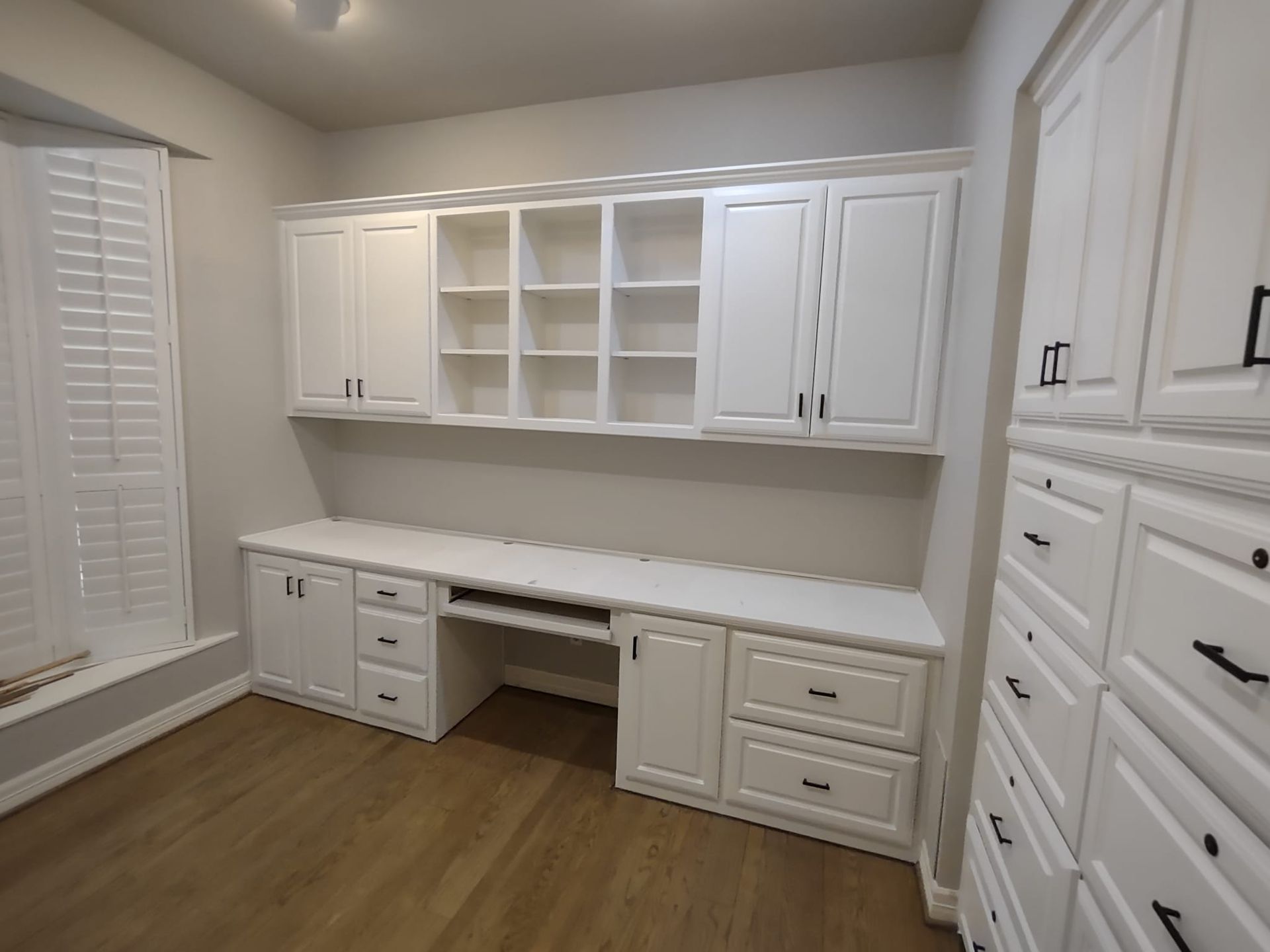 A room with white cabinets and drawers and a desk.