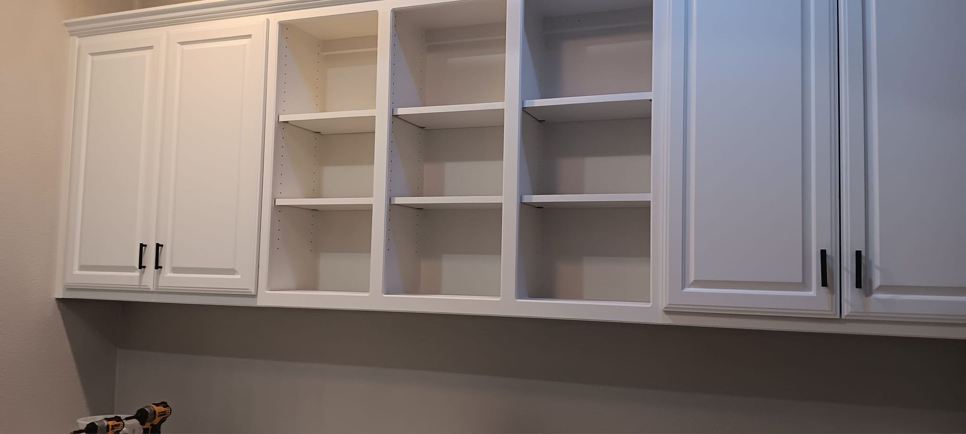 A kitchen with white cabinets and shelves and a desk.
