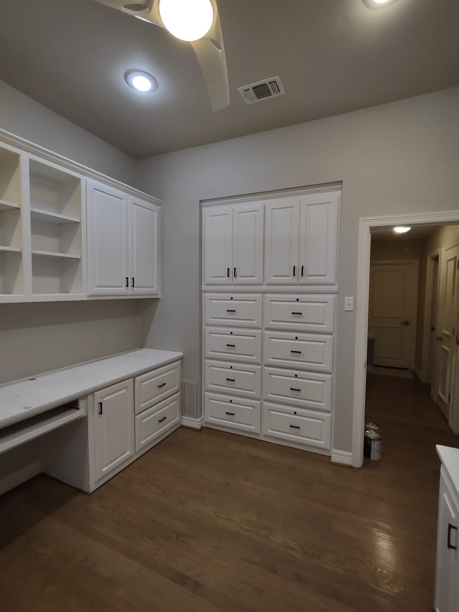 A room with white cabinets and drawers and a desk.