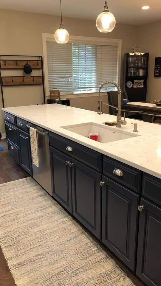 A kitchen with blue cabinets , white counter tops , a sink and a dishwasher.