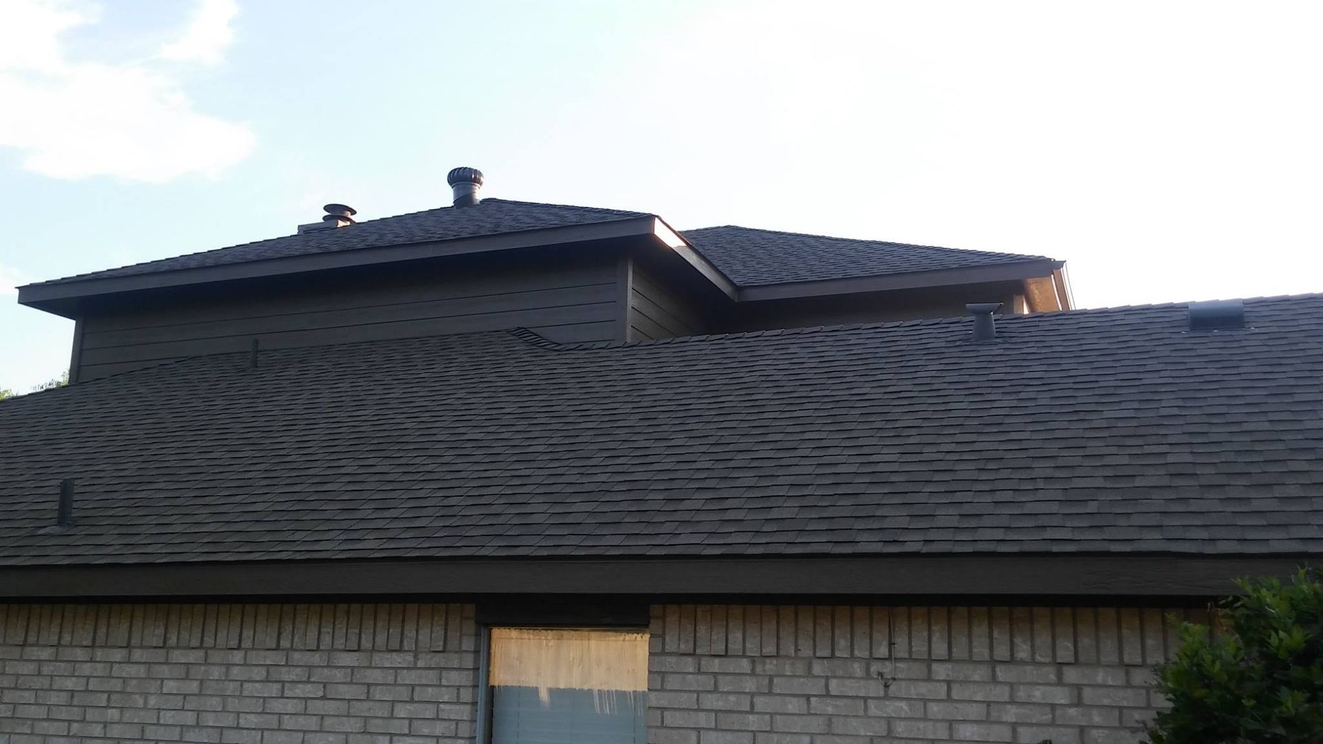 A brick house with a gray roof and a window.