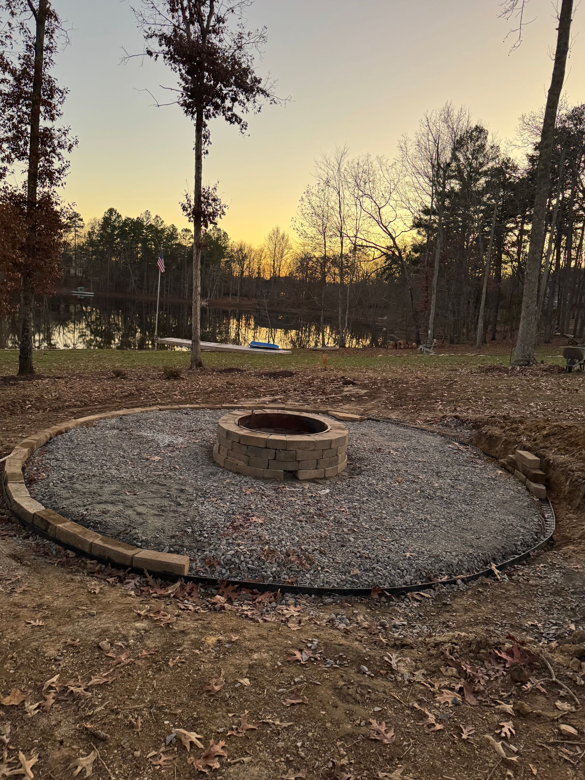 A fire pit is surrounded by gravel and trees in the middle of a field.
