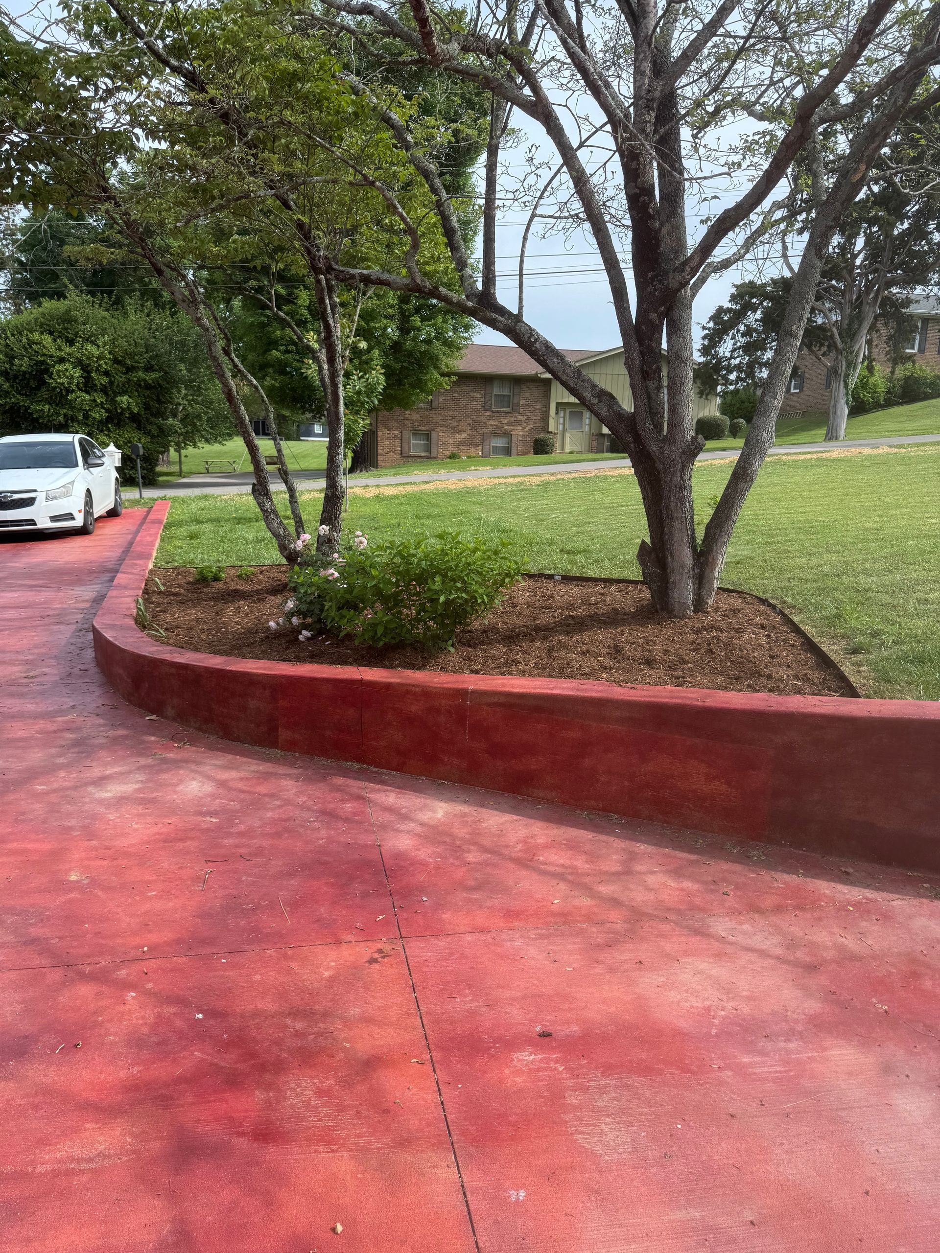 A white car is parked on a red driveway next to a tree.