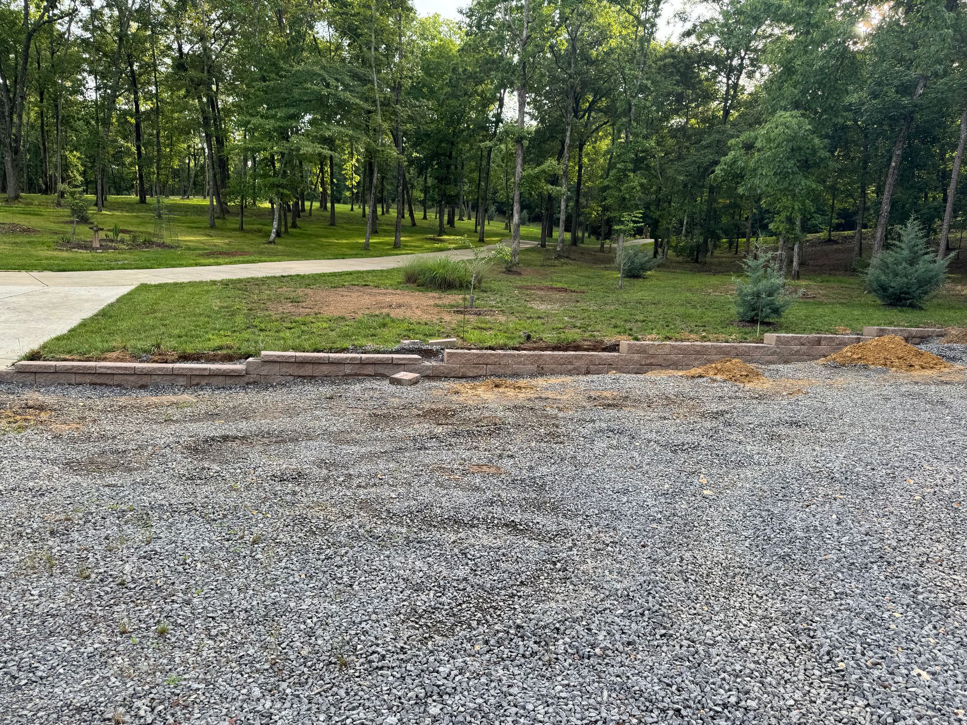 A gravel driveway leading to a park with trees in the background.