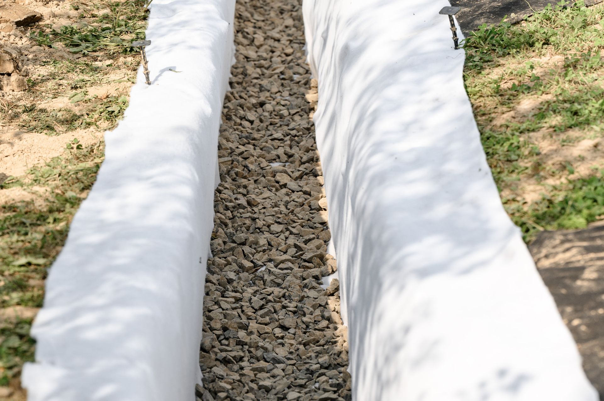 A white tarp is covering a trench filled with gravel.