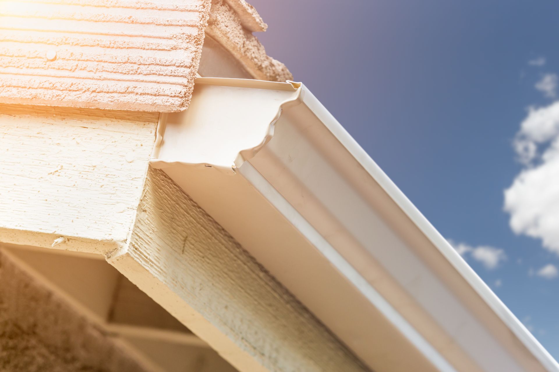 A white gutter on the side of a house with a blue sky in the background.