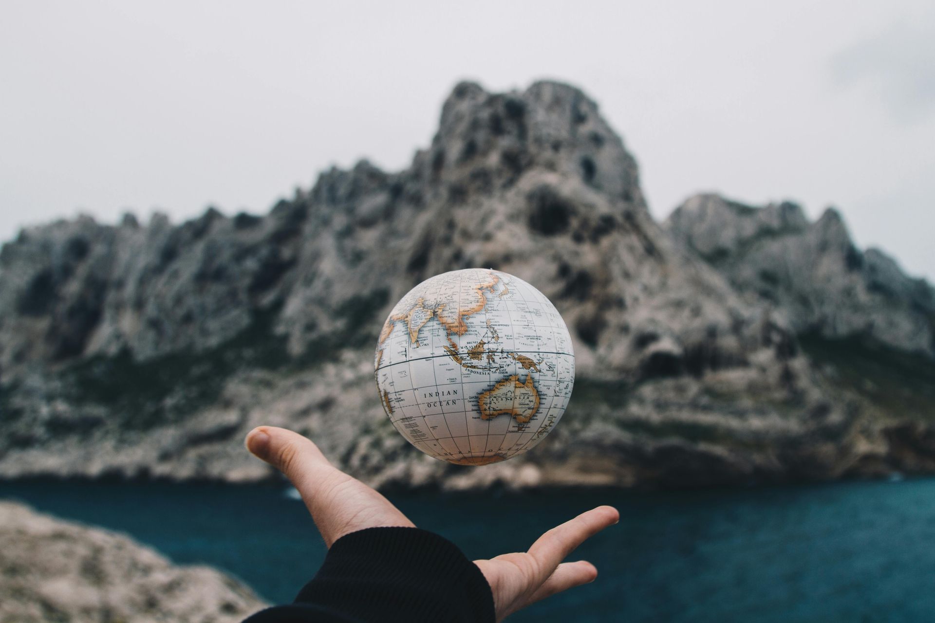 A person is holding a globe in their hand in front of a mountain.