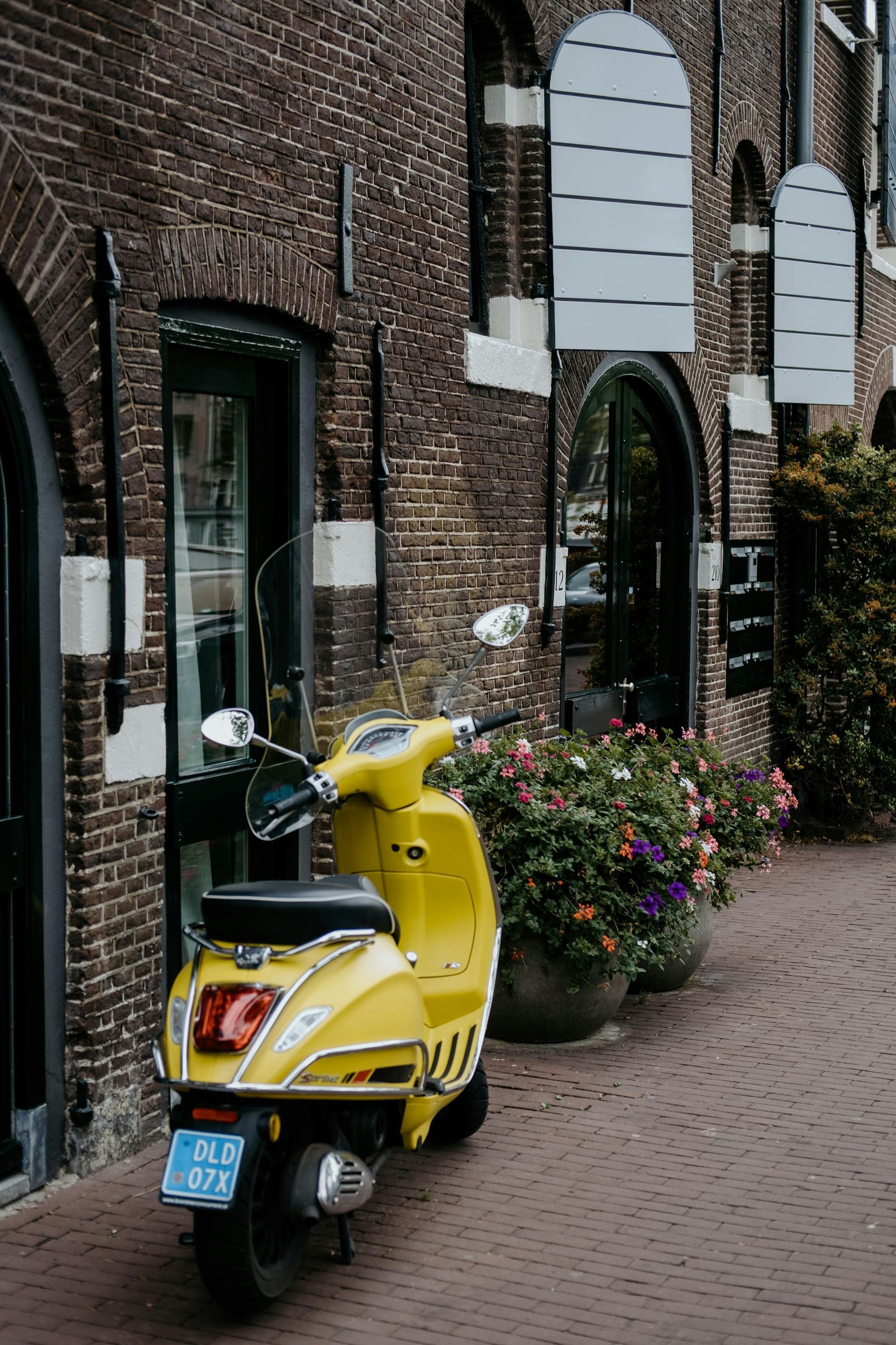A yellow scooter is parked in front of a brick building.