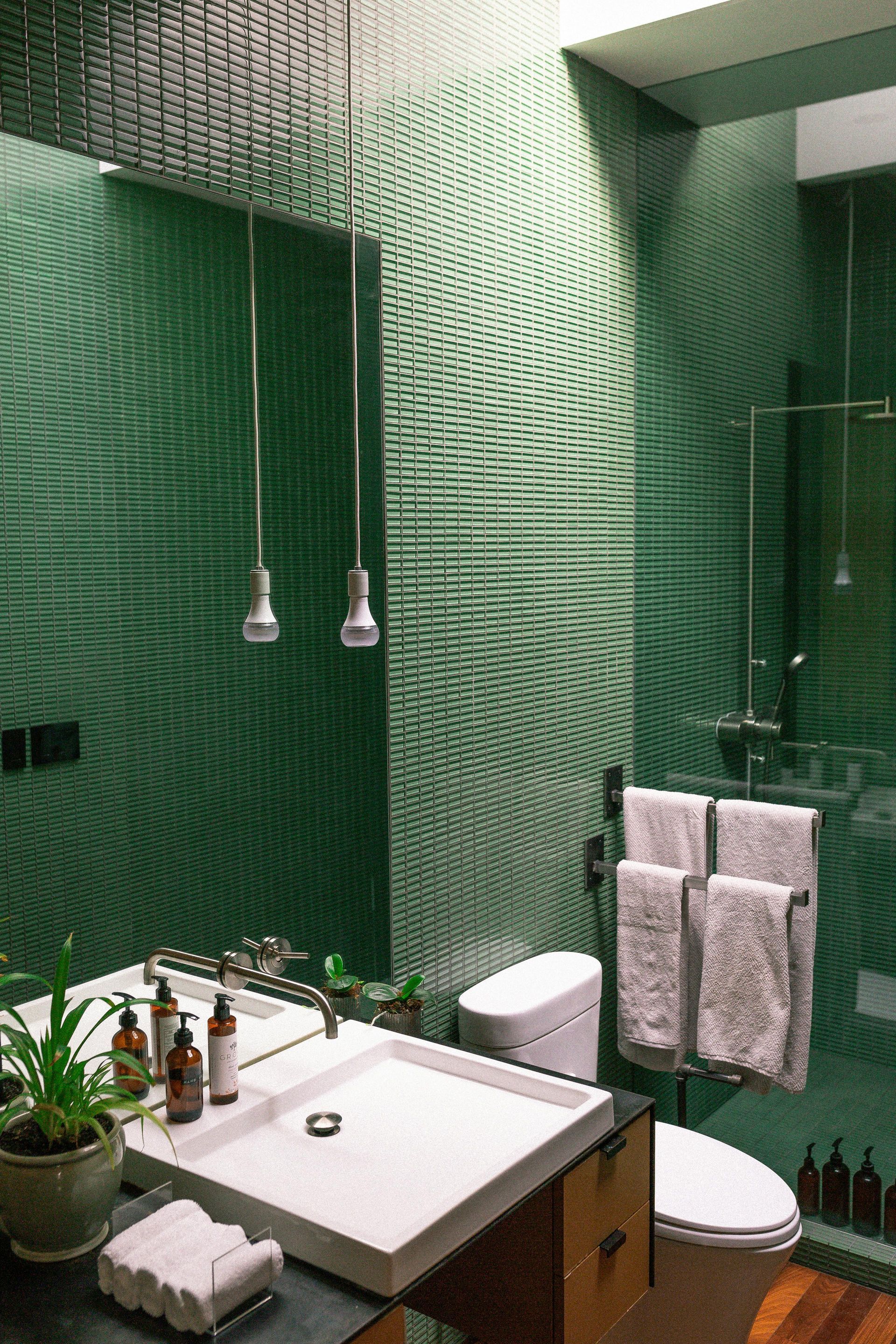 A bathroom with green tiles , a sink , toilet and shower.