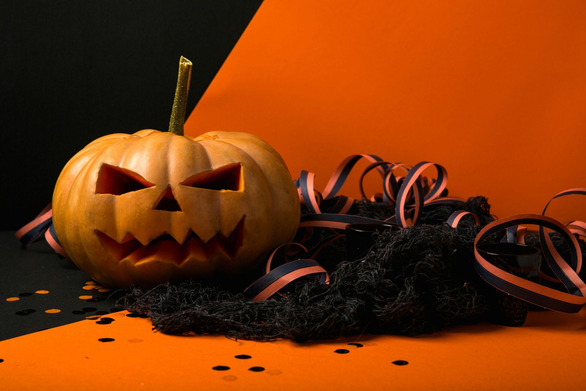 A halloween pumpkin with a face carved into it is sitting on top of a pile of confetti.
