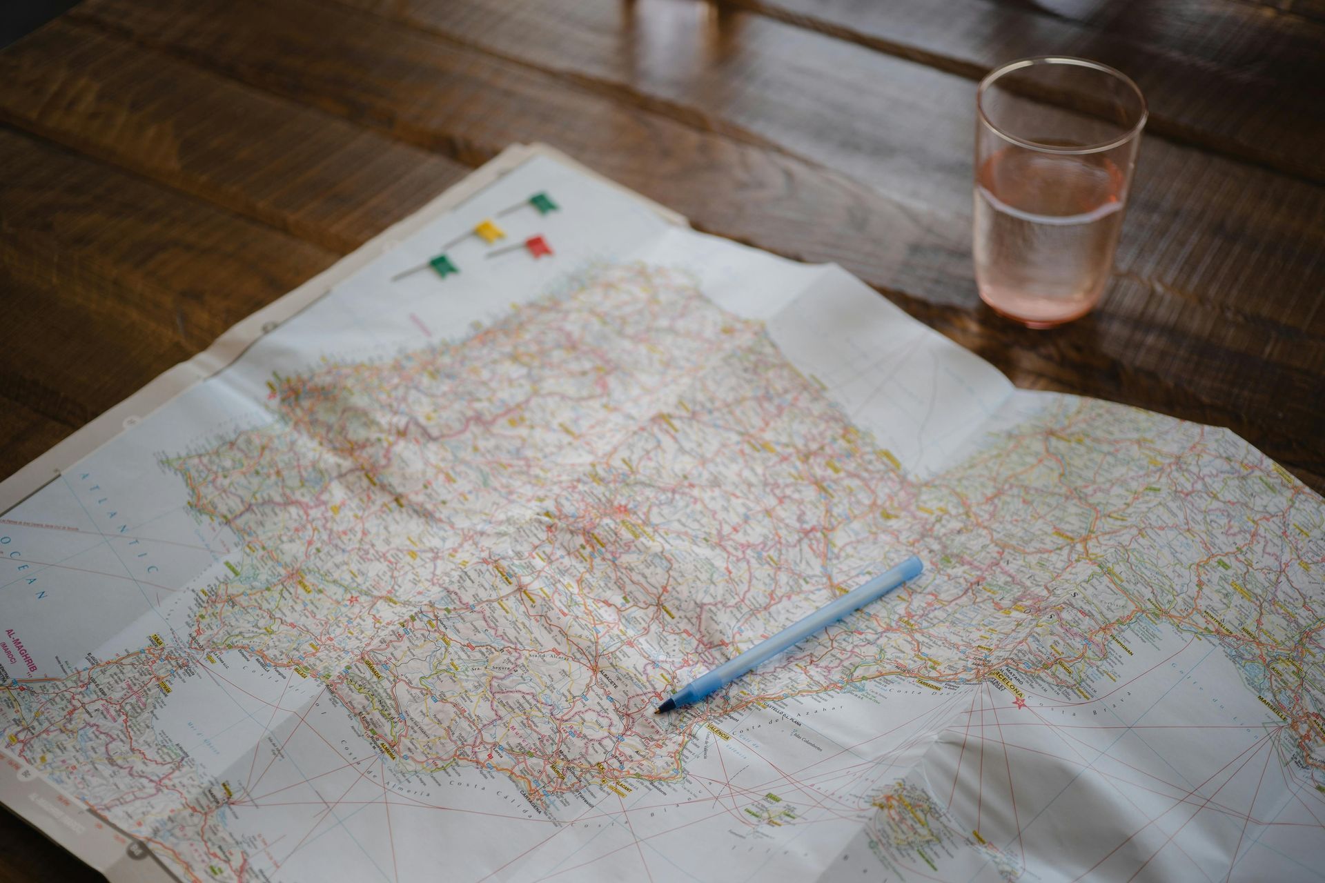 A map with a pen and a glass of water on a wooden table.