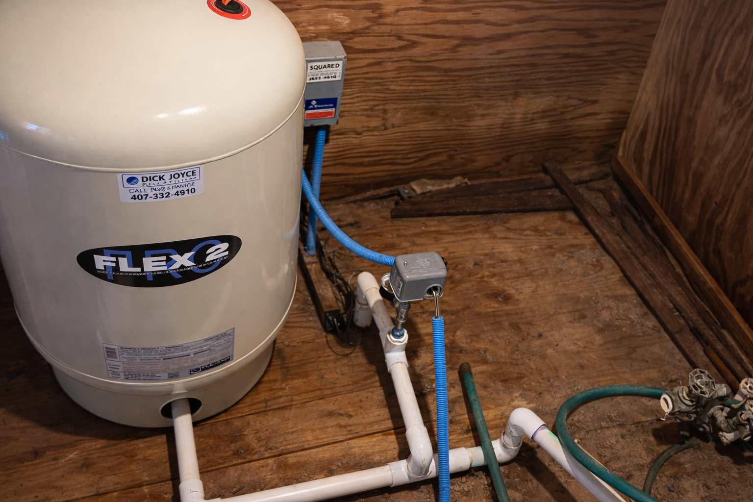 A beige Flex-Lite water pressure tank connected to white PVC pipes and a pressure switch in a room with a wood floor.