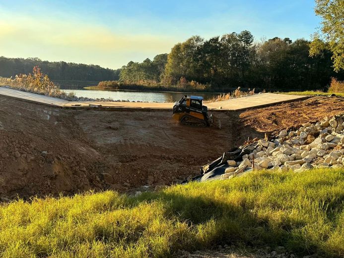 A bulldozer is working on a dam next to a lake.