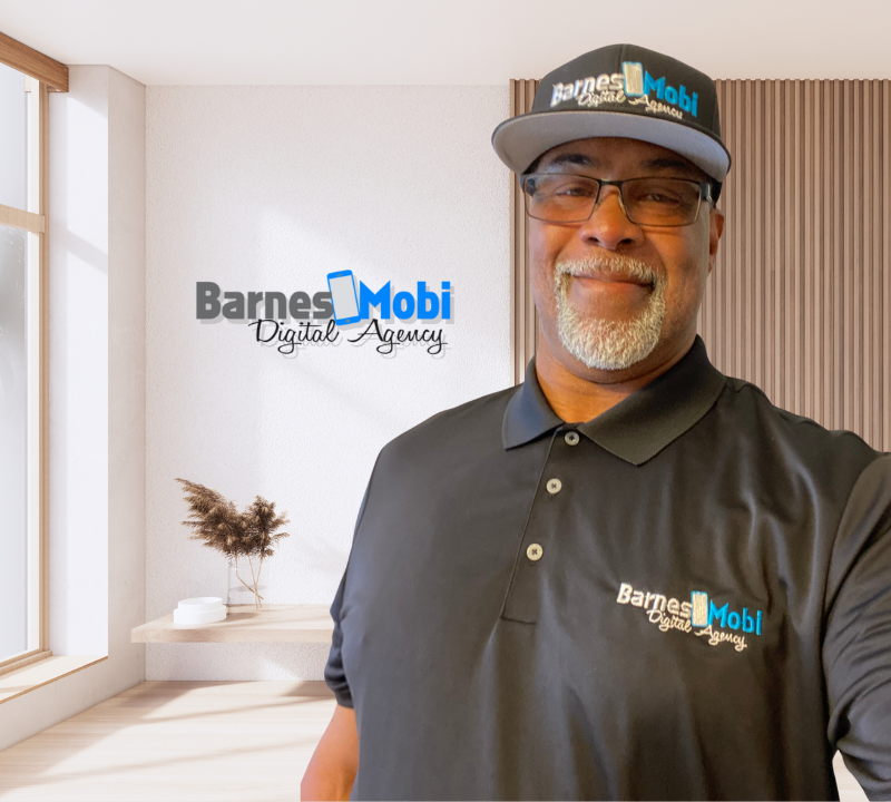 A man wearing a hat and glasses is standing in front of a wall that says barnes mobi digital agency