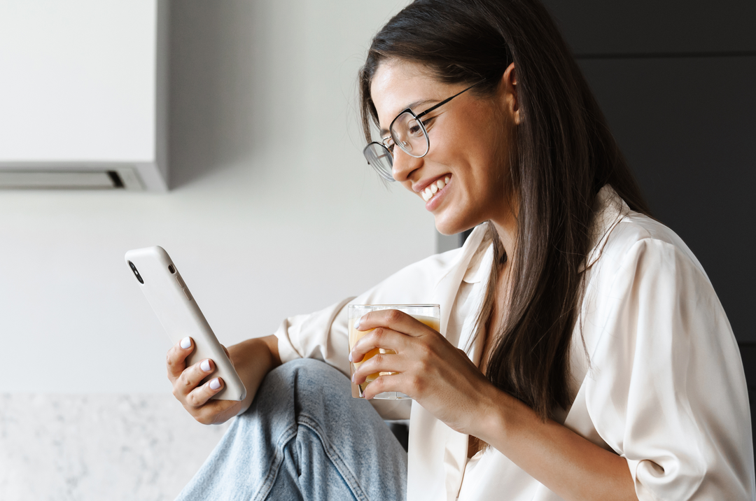 A woman is sitting on the floor using a tablet and drinking coffee.