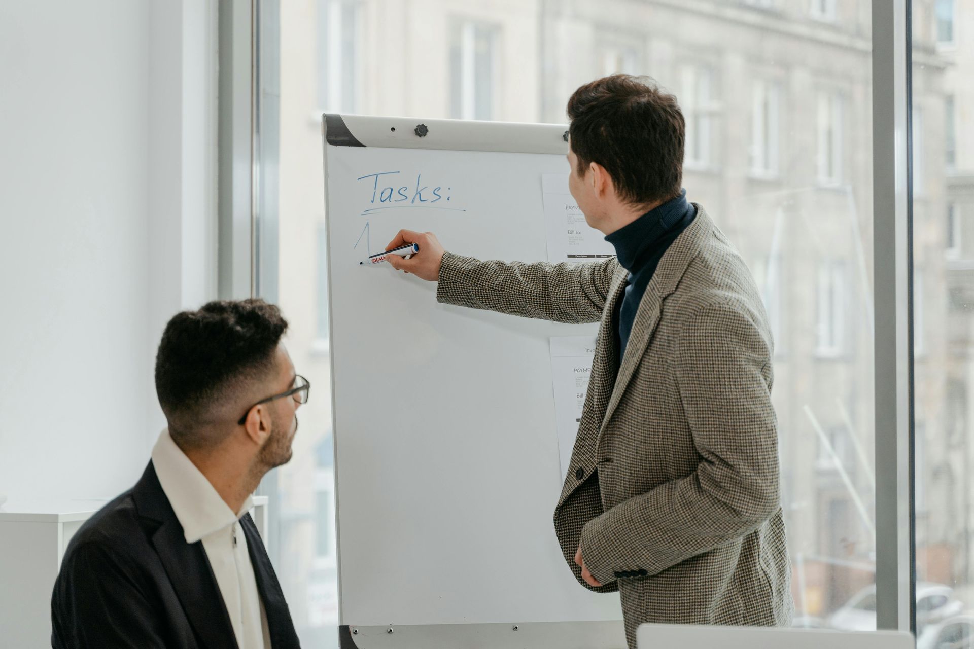Two men are standing next to each other in front of a whiteboard.