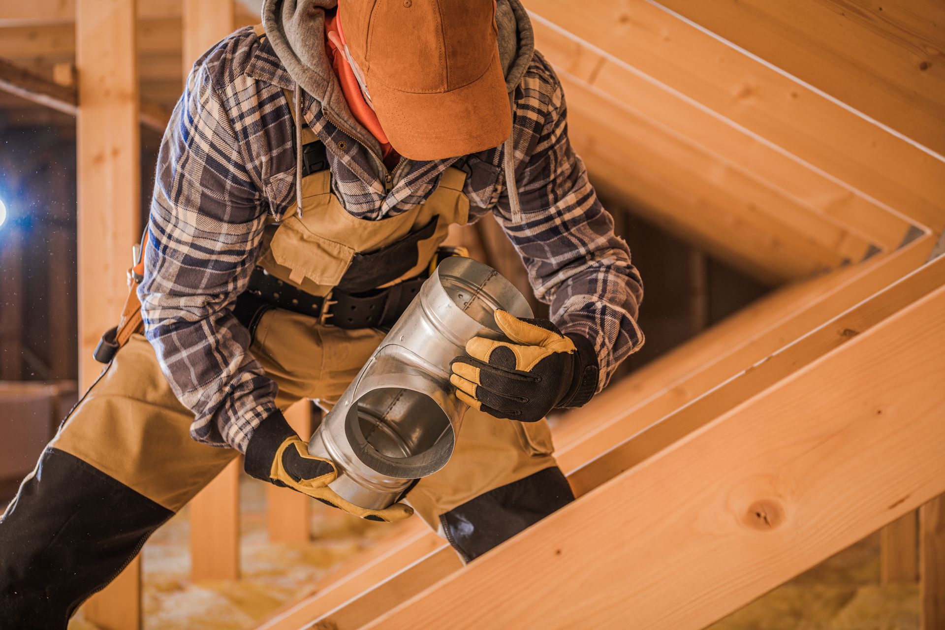 Worker using a circular saw on a wooden roof beam inside an attic under construction