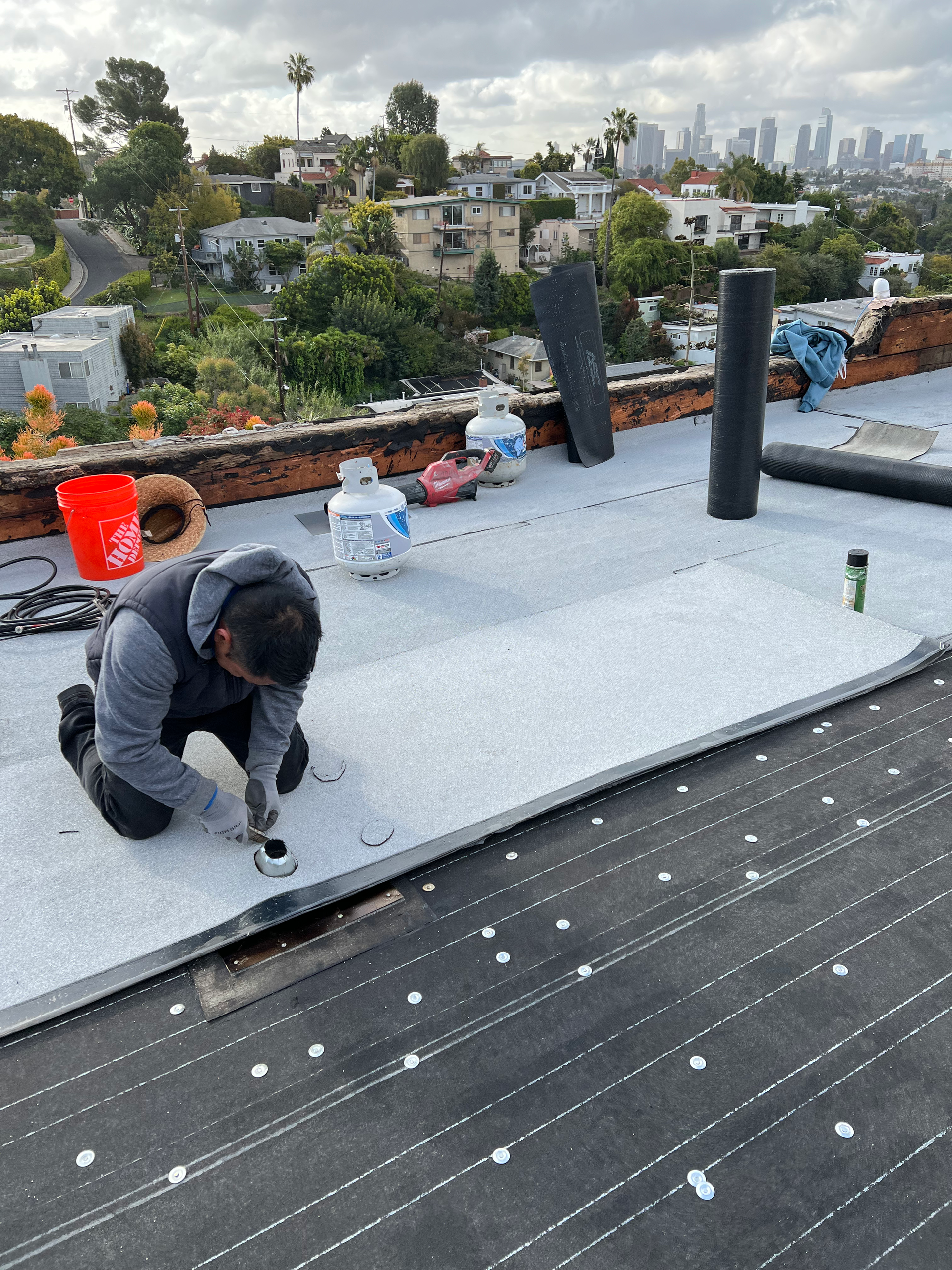 A man is working on a roof with a city in the background.