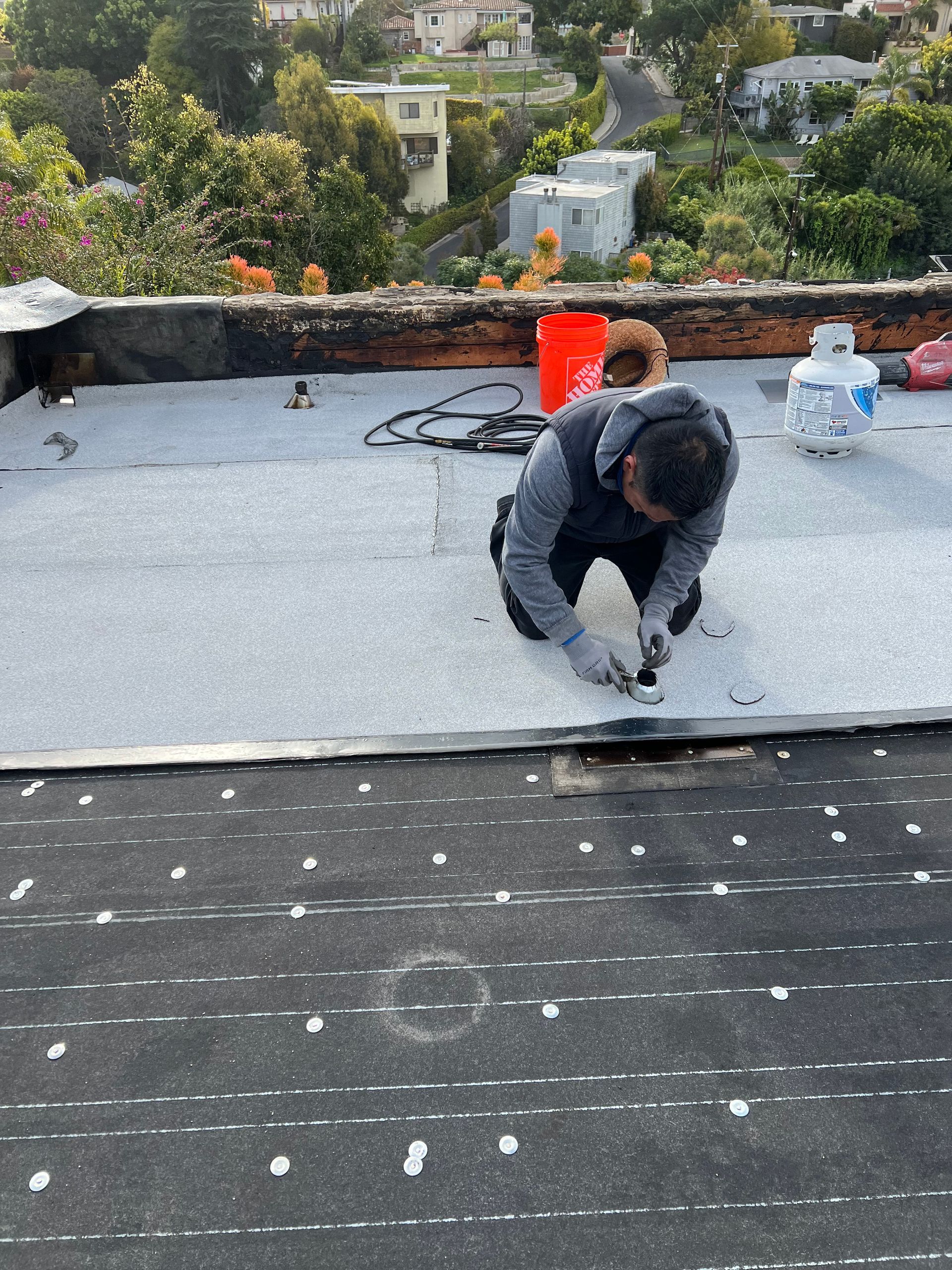 Un uomo sta lavorando su un tetto con un secchio sullo sfondo.