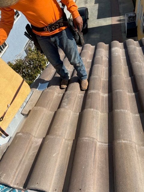 A man is working on a roof with a toolbox next to him.