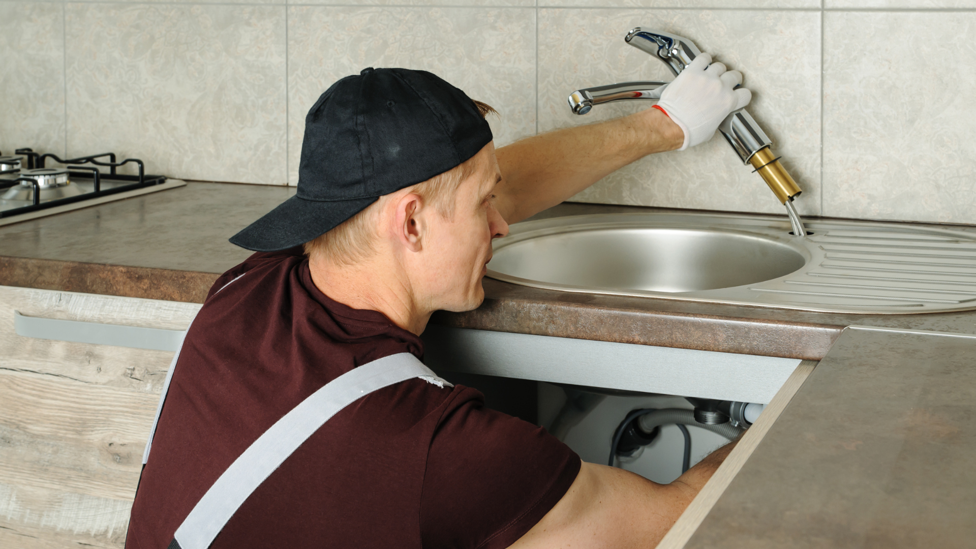 A man is fixing a sink in a kitchen with a wrench.