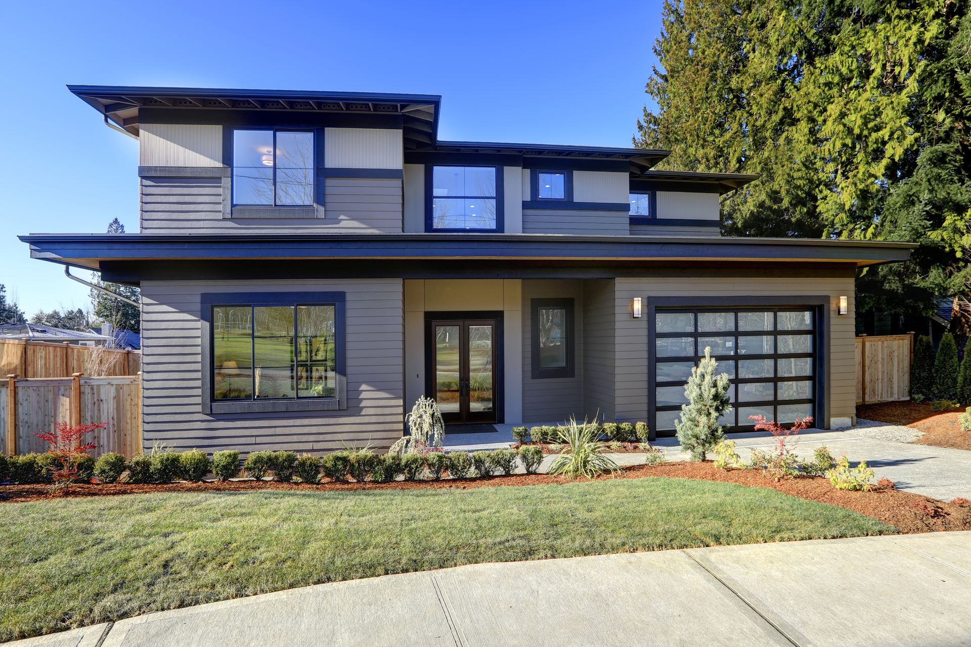 Une maison moderne avec un grand garage et une pelouse verte luxuriante.