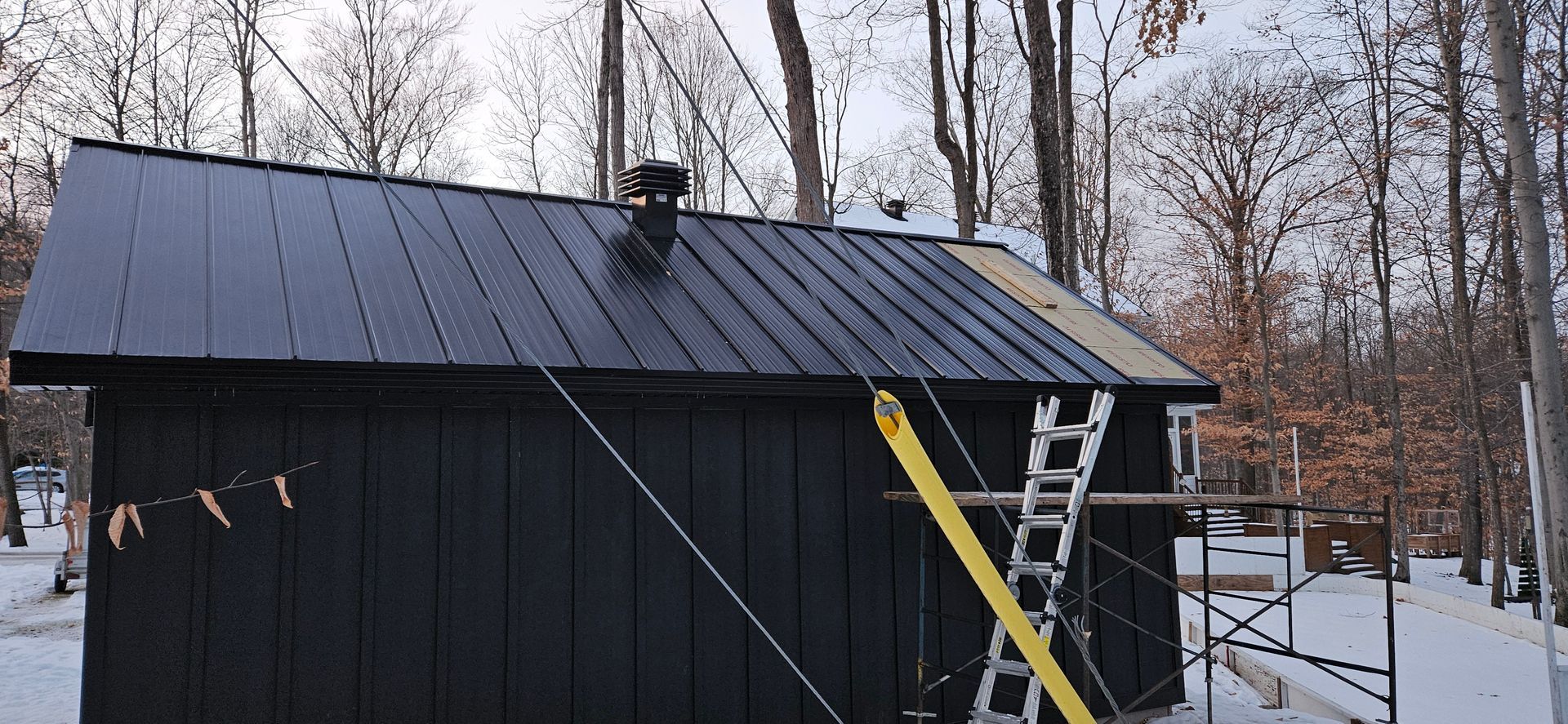 Un hangar noir avec un toit en métal est en cours de construction dans la neige.