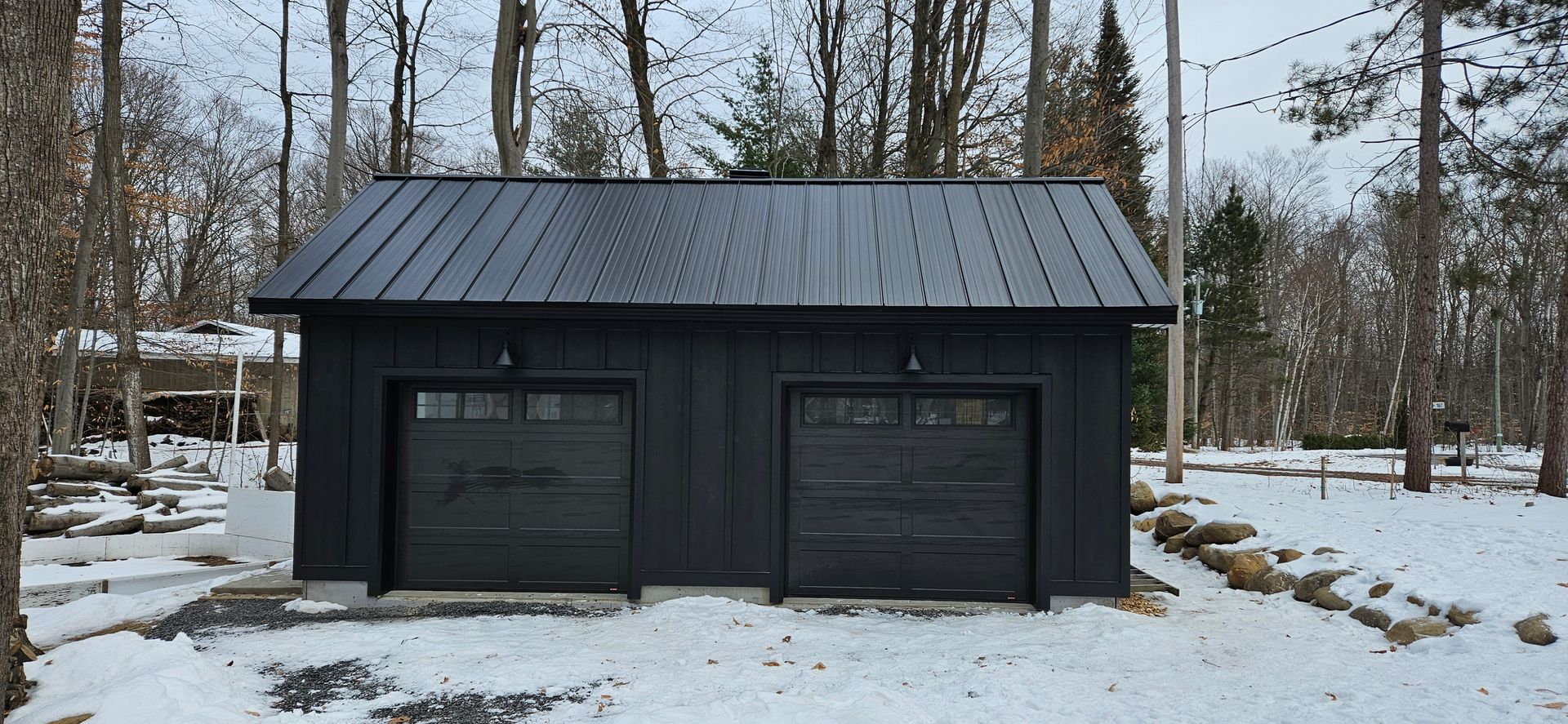 Un garage noir avec deux portes de garage est assis dans la neige.