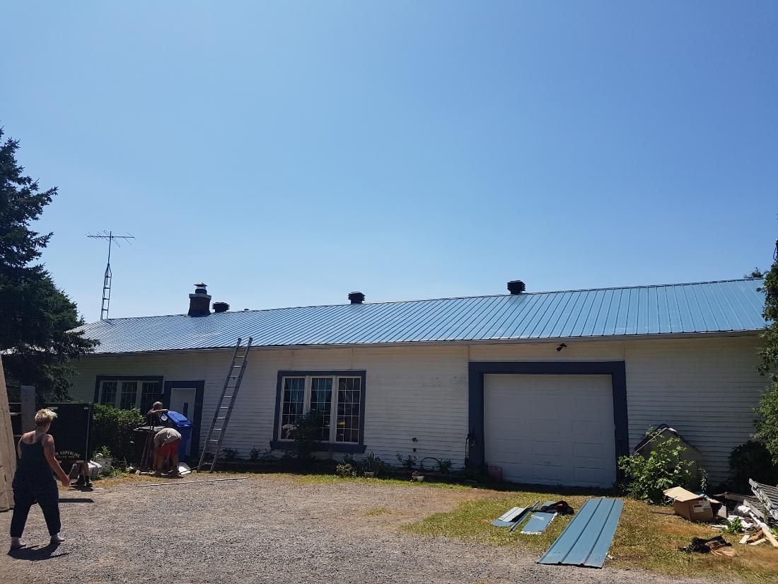 Un homme se tient devant une maison blanche avec un toit bleu.