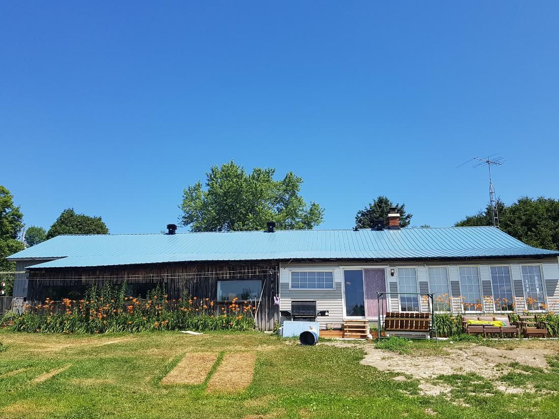 Une grande maison au toit bleu se trouve au milieu d'un champ herbeux.