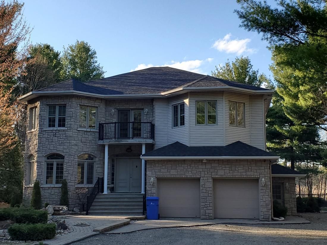 Une grande maison au toit noir est entourée d'arbres.
