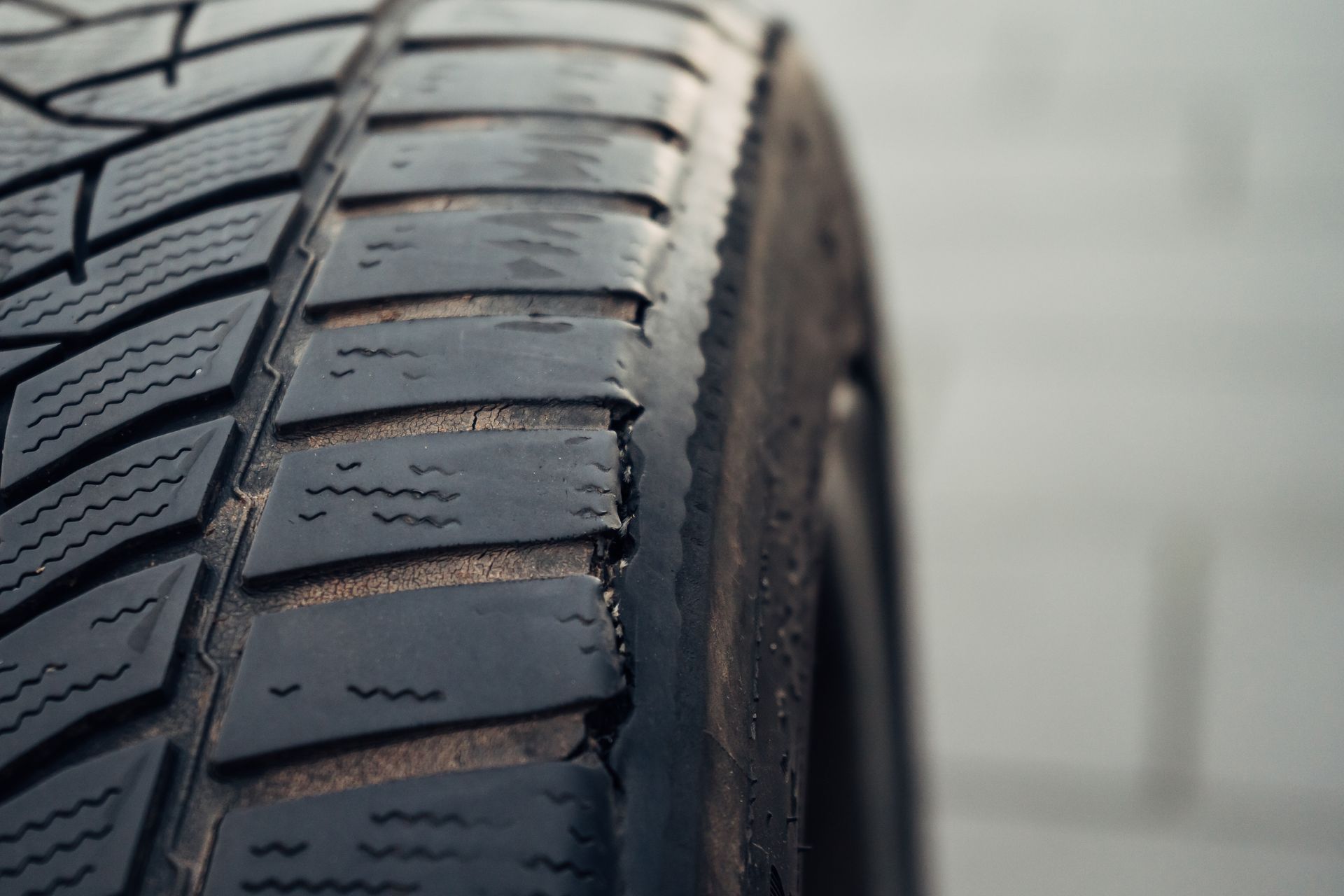 Close-up of a worn car tire showing cracks and wear on the rubber tread.
