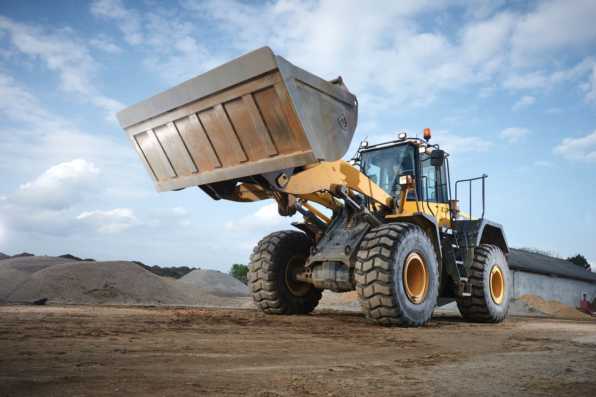 Yellow and black front-end loader with raised bucket on a construction site, blue sky in background.