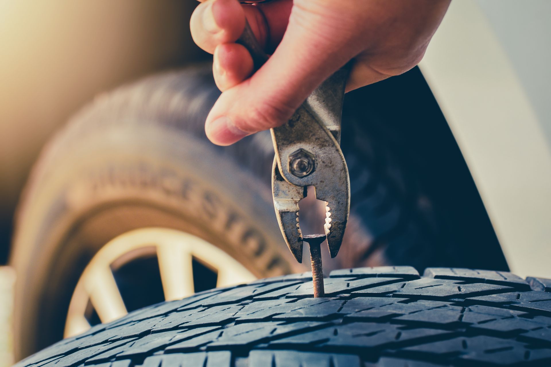 Hand removing a staple from a car tire with pliers.
