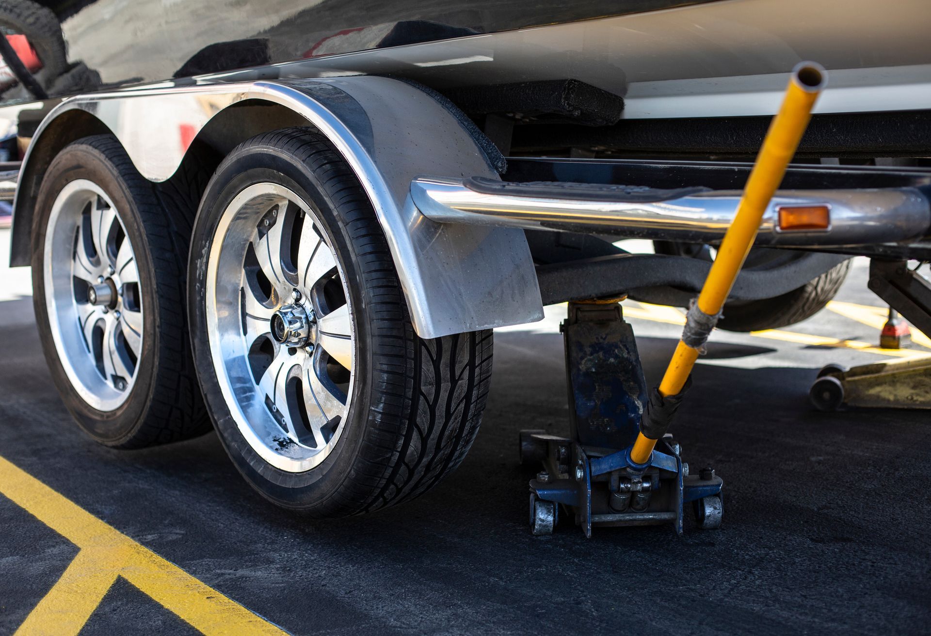 Trailer tire being changed with a jack on a paved surface.