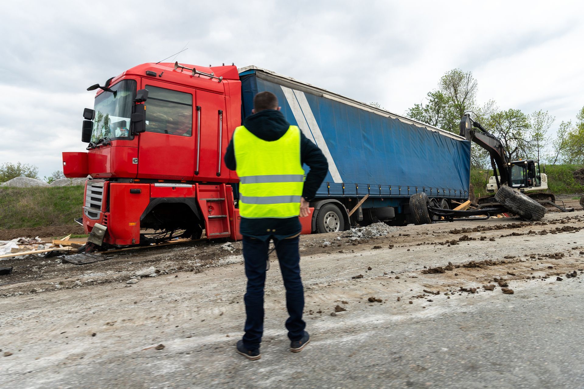 Man in yellow vest observes a red truck stuck in mud near an excavator.