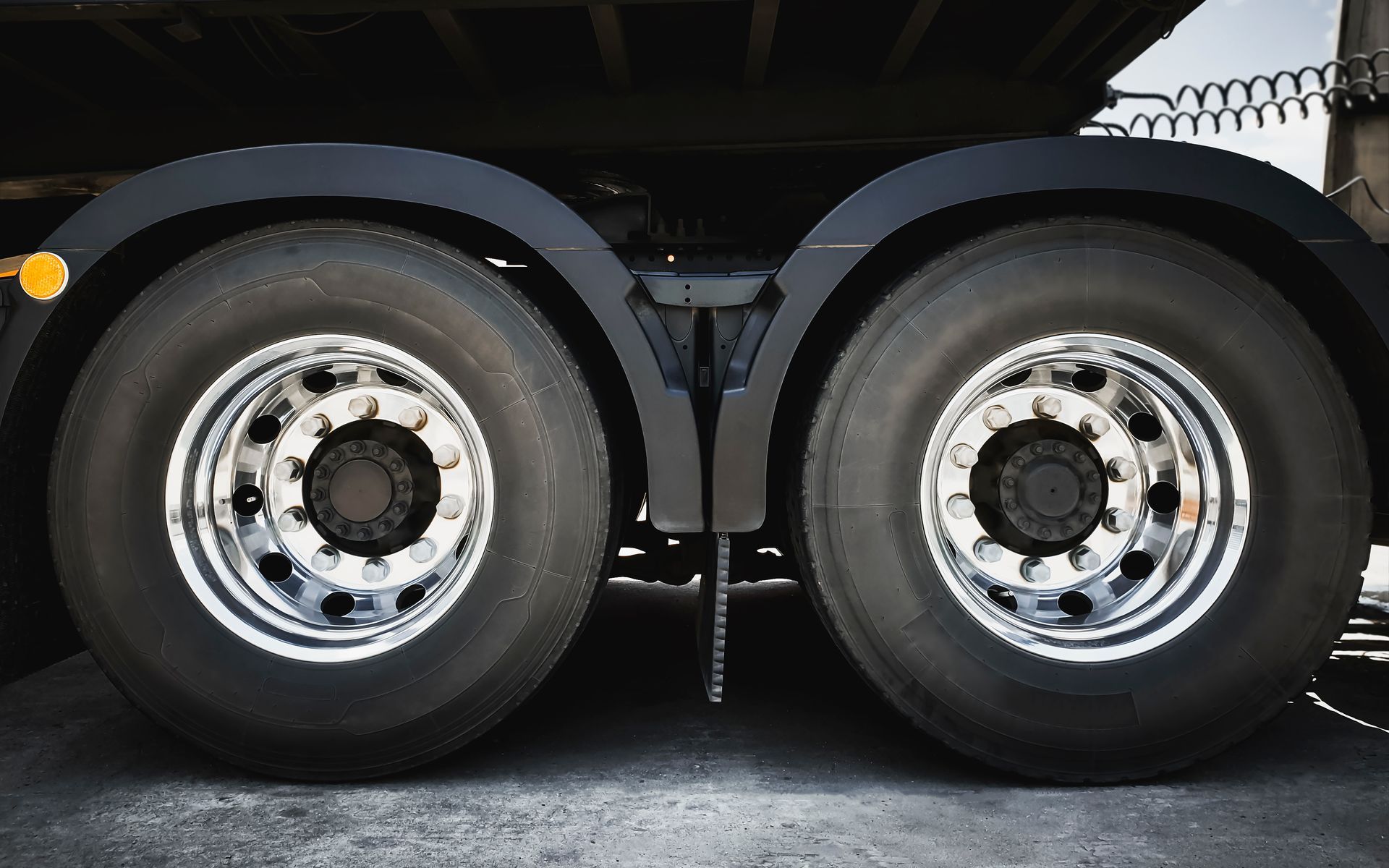 Two black truck tires with chrome rims under a black fender.
