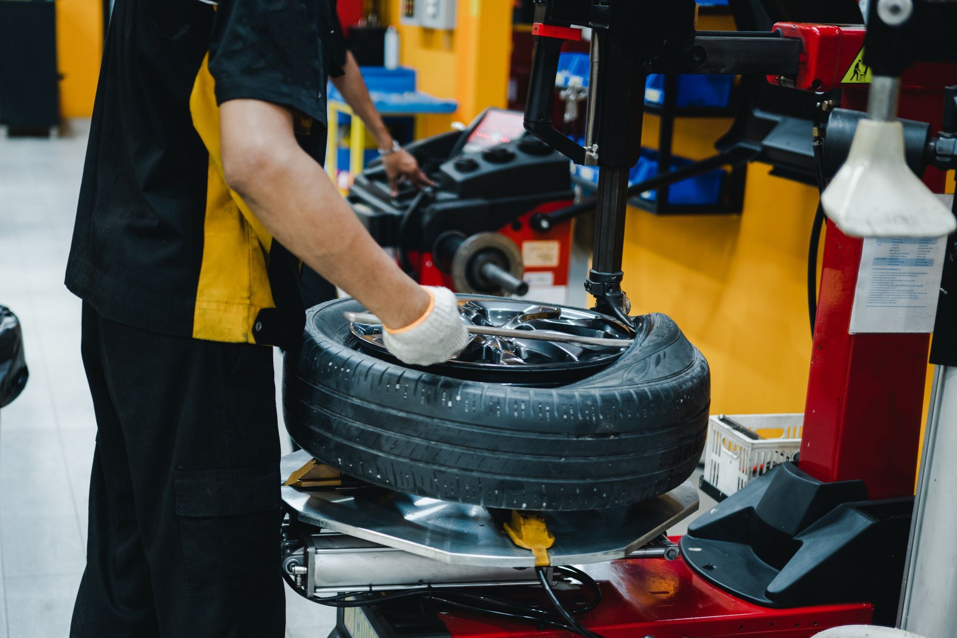 Mechanic working on a tire using a machine in a service bay, wearing gloves.